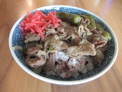 ほかほかご飯の上に、つゆだくの牛肉、玉ねぎ、ししとう、紅ショウガをたっぷりと盛り付けた特製牛丼の完成写真