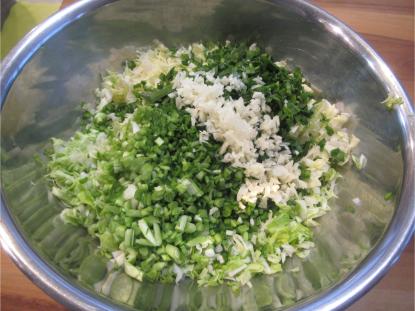 ボウルいっぱいに細かくみじん切りにされたキャベツ、にら、にんにくなどの手作り餃子の野菜材料